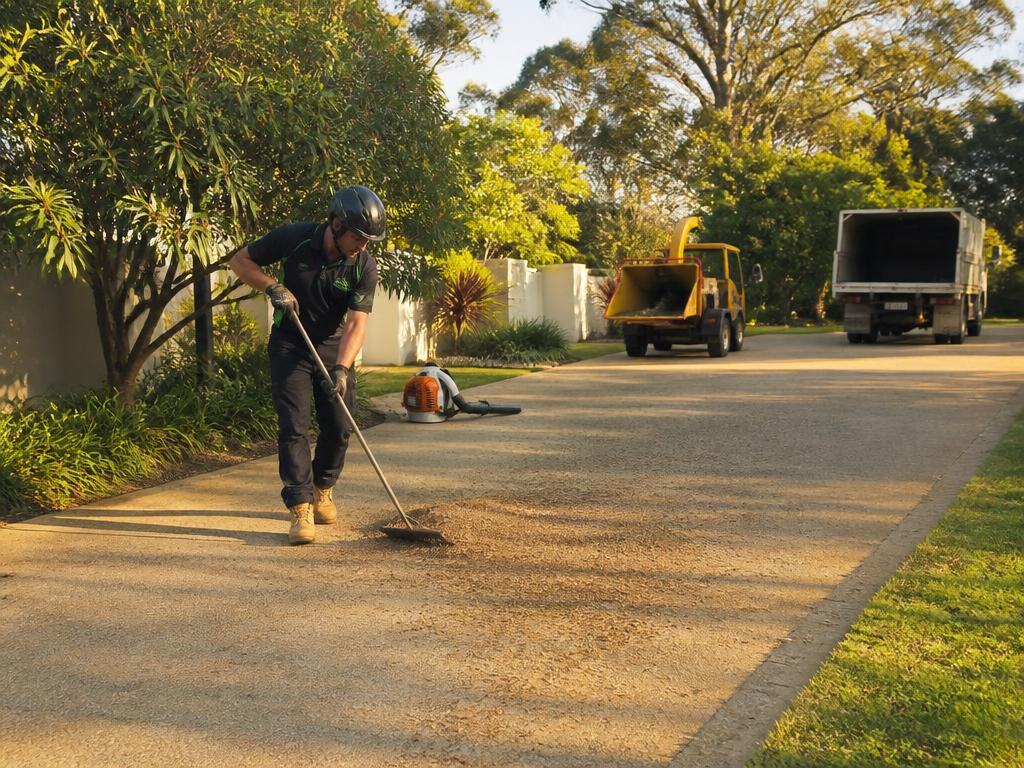 Arborist sweeping wood chips off a driveway inside a coned exclusion zone after the job